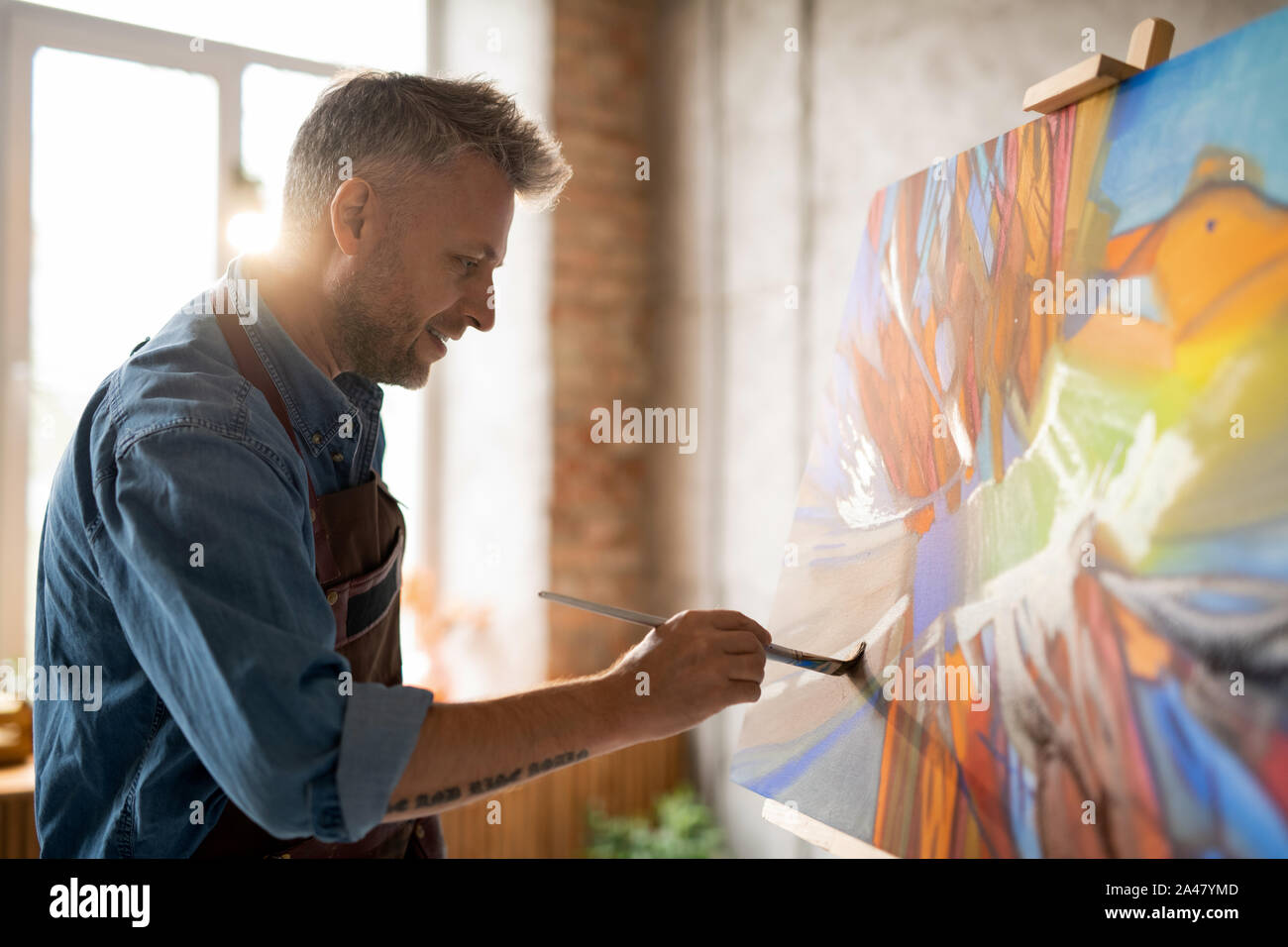 Happy mature master of arts in apron working over abstract painting Stock Photo