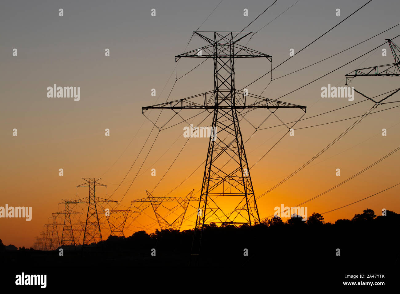 The sun rising behind a pair of towering electricity pylons Stock Photo