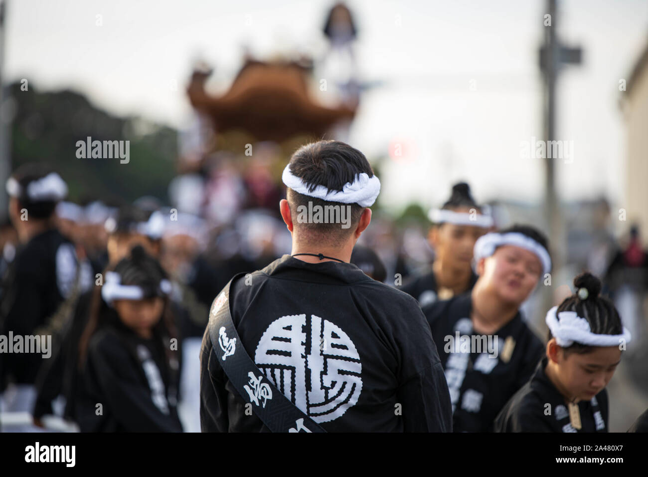 Man wearing white headband and black happi oversees danjiri procession at local Japanese festival Stock Photo