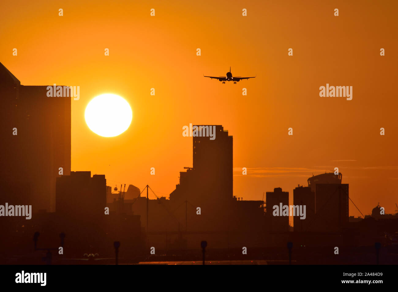 Plane landing at London City airport with golden skies as the sun sets behind the Canary Wharf skyline Stock Photo