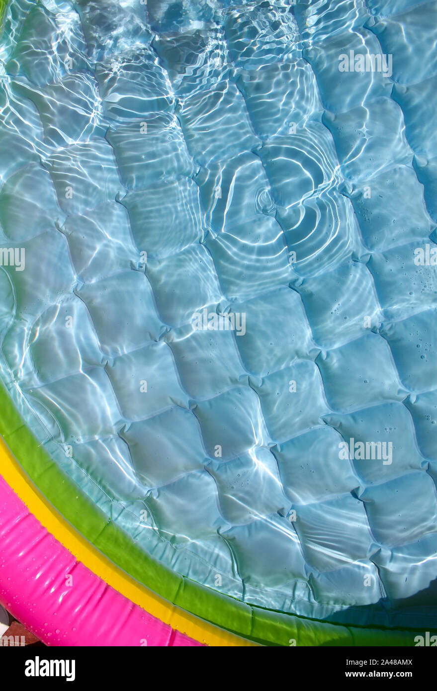 Bright blue inflatable paddling pool surface with water ripples. Summer