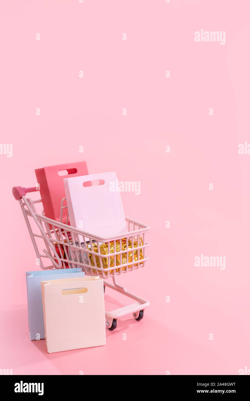 Annual sale shopping season concept - mini pink shop cart trolley full of paper bag gift isolated on pale pink background, blank copy space, close up Stock Photo