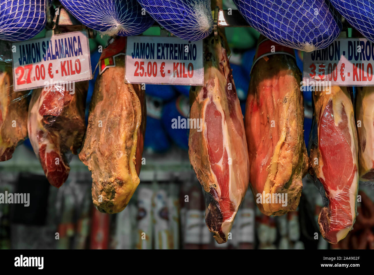 Whole bone-in legs of Spanish serrano iberico ham on display with price tags with the ham names at a butcher shop in a local market Madrid, Spain Stock Photo