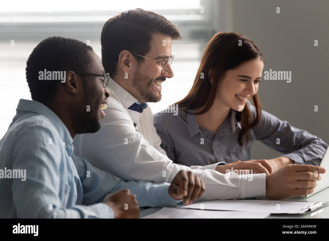 Overjoyed multiracial teammates watching funny video together. Stock Photo