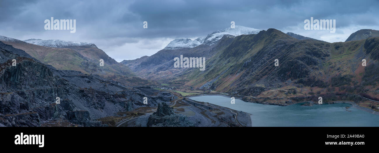 Stunning landscape image of Dinorwig Slate Mine and snowcapped Snowdon mountain in background during Winter in Snowdonia with Llyn Peris in foreground Stock Photo