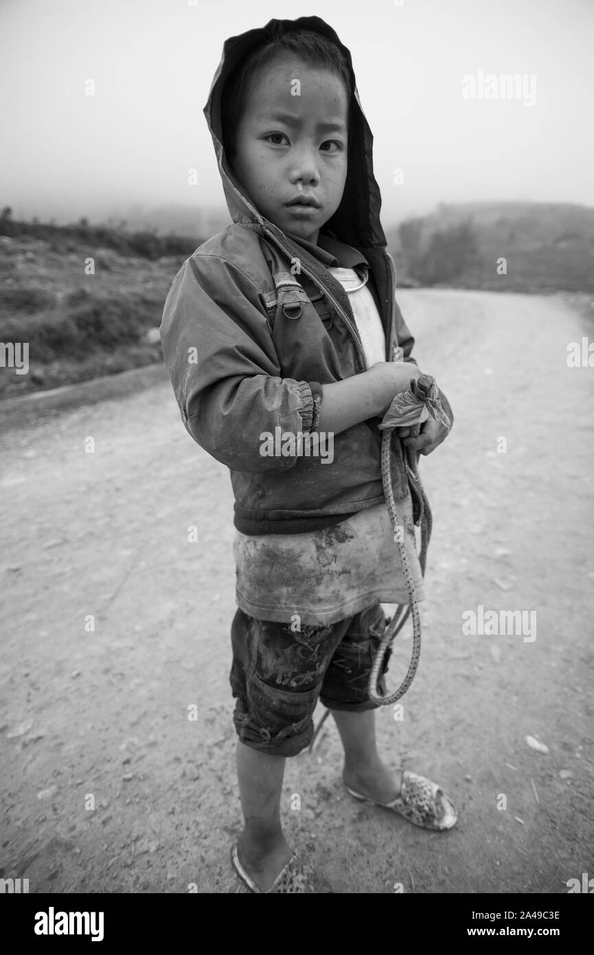 Sapa, Lao Cai, Vietnam - March 14, 2011: Cute Hmong ethnicity kid in a misty road among the mountains of Sapa Stock Photo