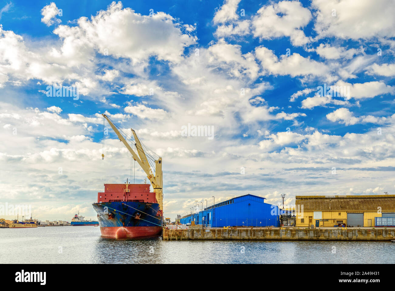 Cargo ship with cranes docked in industrial port Stock Photo