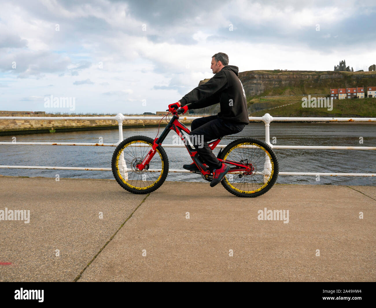 A middle aged man in a black track suit riding an off road sports bicycle on Whitby West Pier Stock Photo
