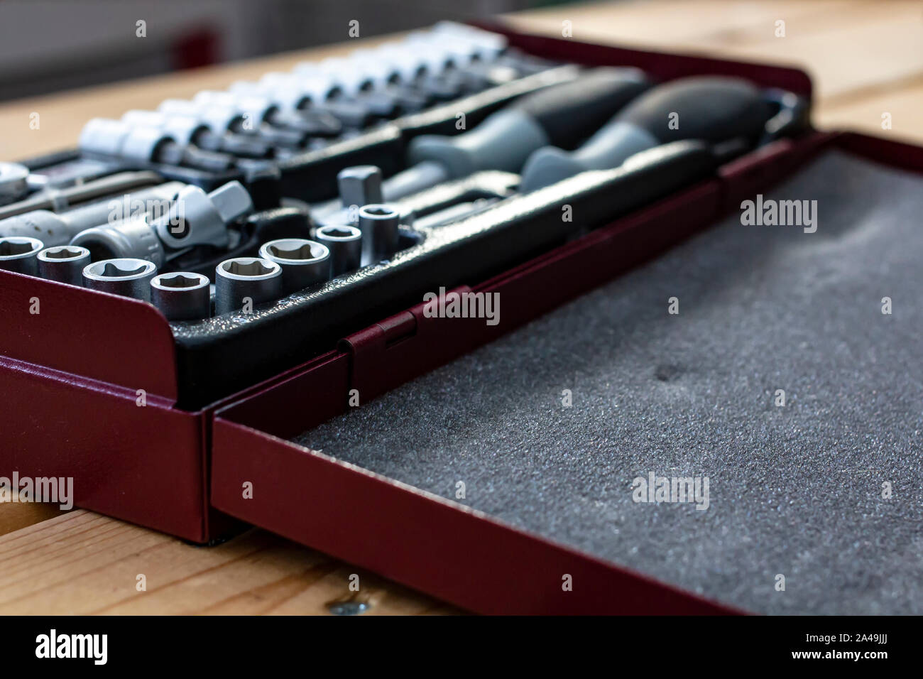 Metallic red box with a set of wrenches lying on a wooden table in natural light. Close-up. Stock Photo