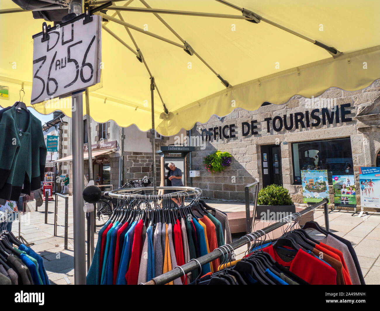 Tourist Office Breton Brittany Street Market clothing stall Office de Tourisme behind  Charming French Breton outdoor street weekly general market in church square selling local produce like meats cheeses clothing drinks basketware etc in Névez Brittany France Stock Photo