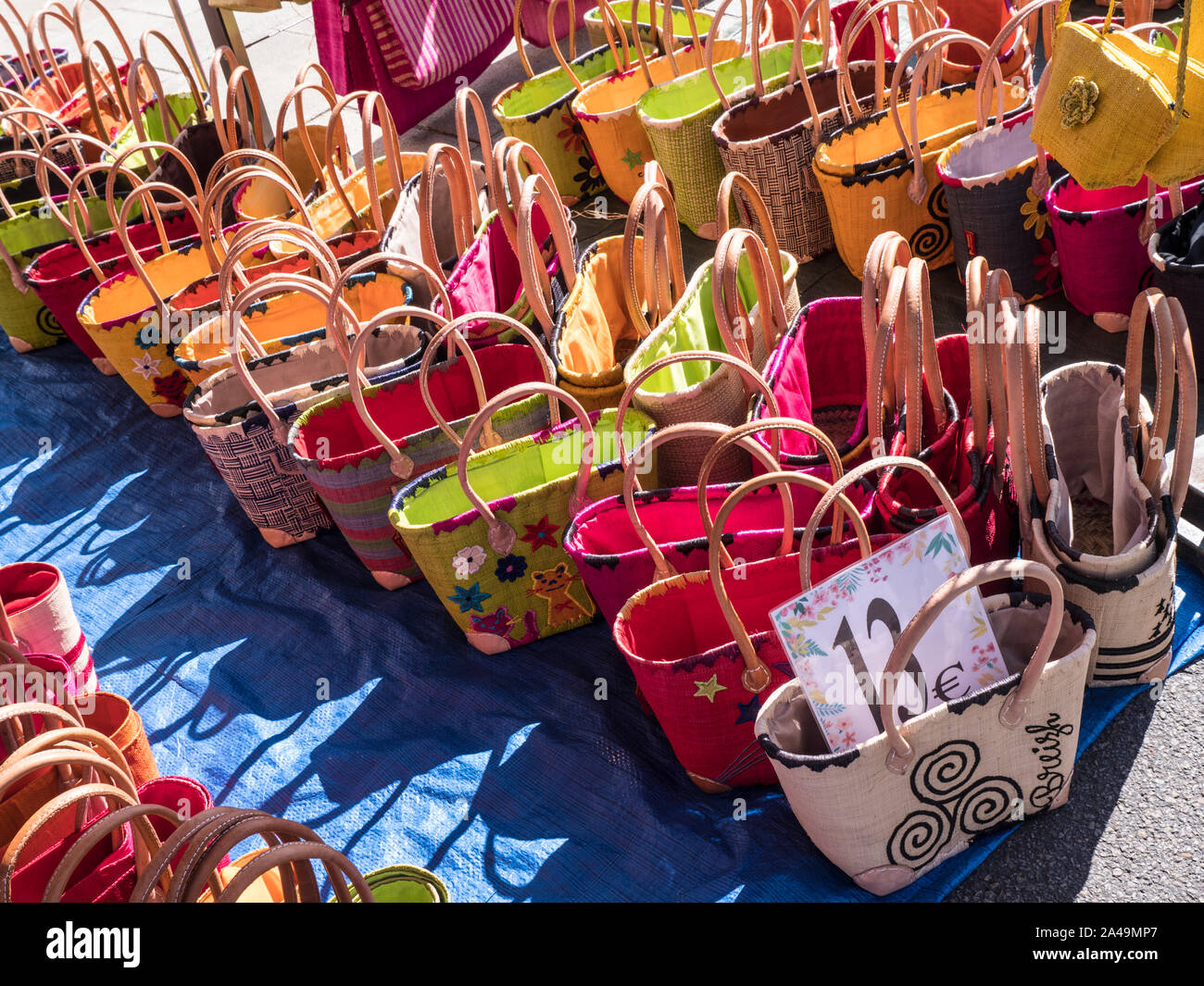 BASKETWARE SHOPPING BAGS MARKET 13€ DISPLAY OUTDOORS SUNLIT Breton Nevéz Brittany Street Market Charming French Breton weekly general market in church square selling local produce such as basketware etc in Névez Brittany France Stock Photo