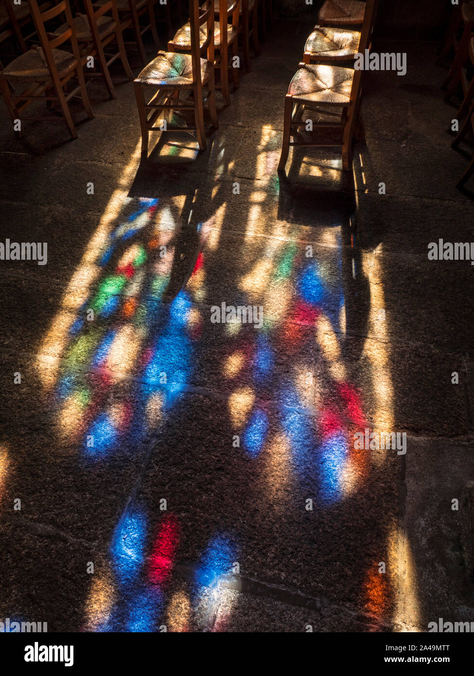 Faith contemplation Church stain glass window colourful late afternoon sunset light window pattern projected on to church chairs pews and flag stone floor in peaceful contemplative faith religious environment Stock Photo