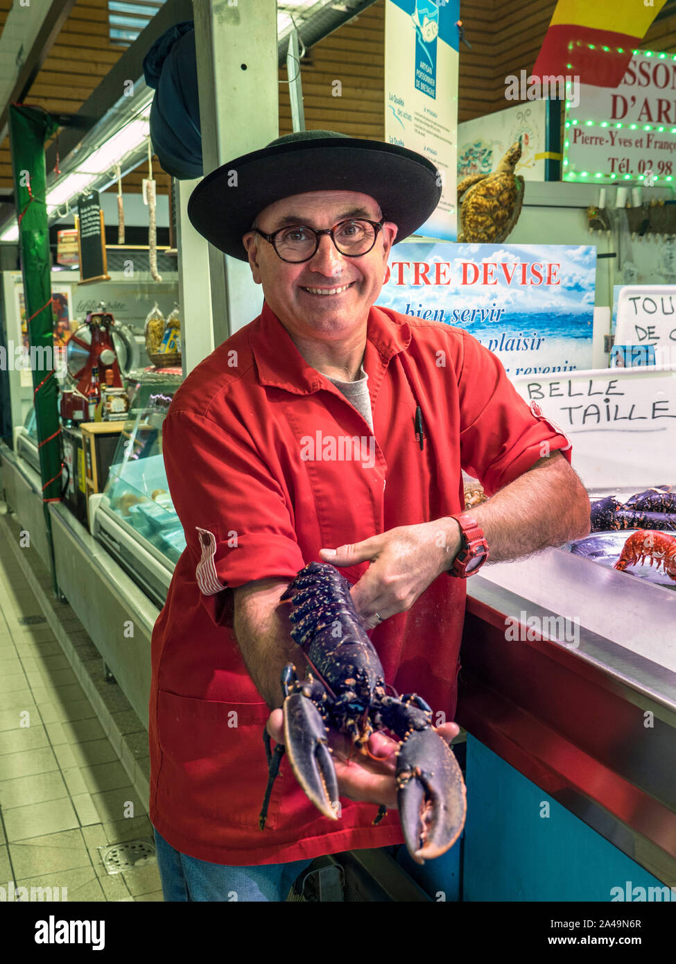 BLUE LOBSTER FRANCE BRETON FISHMONGER HOMARD BLEU FISH MARKET STALL CONCARNEAU FRANCE BRITTANY  Concarneau daily interior French Fish Market hall and character fishmonger, in Breton style outfit proudly displaying his local  live blue lobster for sale Brittany Finistere France Stock Photo