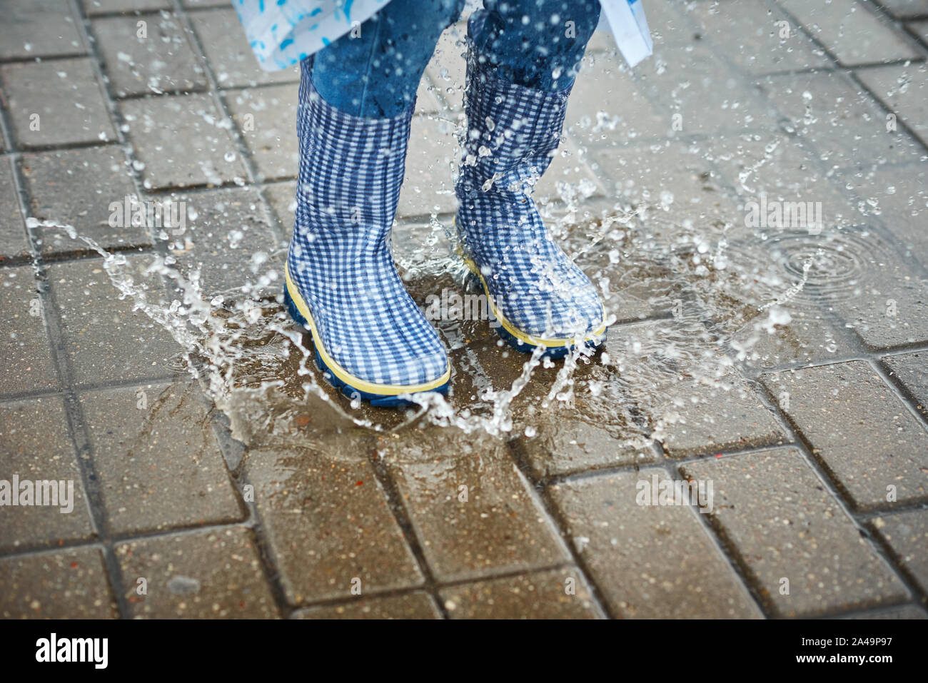 child in blue rubber boots jumping over puddle in the rain Stock Photo ...