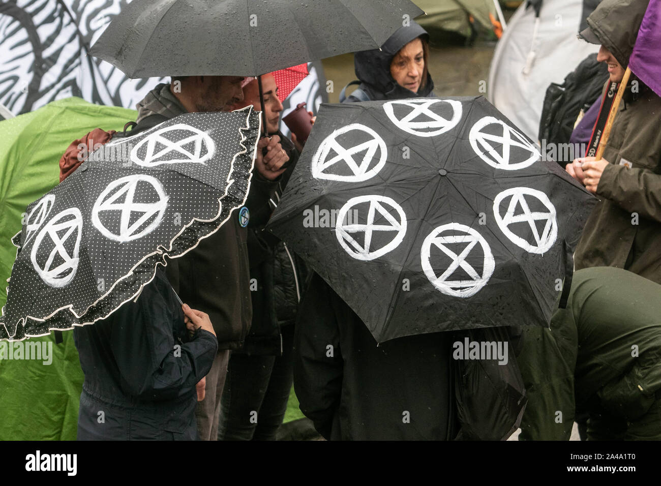 London, UK - 13 October 2019. Climate activists shelter under umbrellas with the Extinction rebellion symbol as they continue their protest for a seventh day while camping  out in Trafalgar Square in an attempt to force the government to declare a climate emergency and meet their demands to reduce to zero carbon emmissions by 2025. Credit: amer ghazzal/Alamy Live News Stock Photo