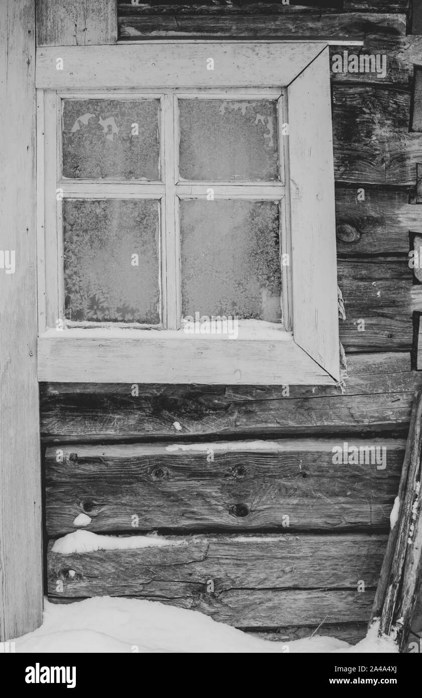 A small window with frost-covered glass in an old log cabin on a winter evening in the village. Close-up. Stock Photo