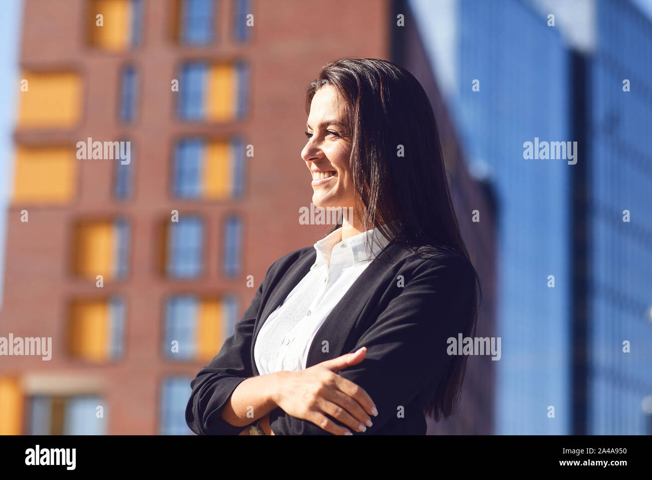 A happy businesswoman is smiling on the background of a business building outdoors. Stock Photo