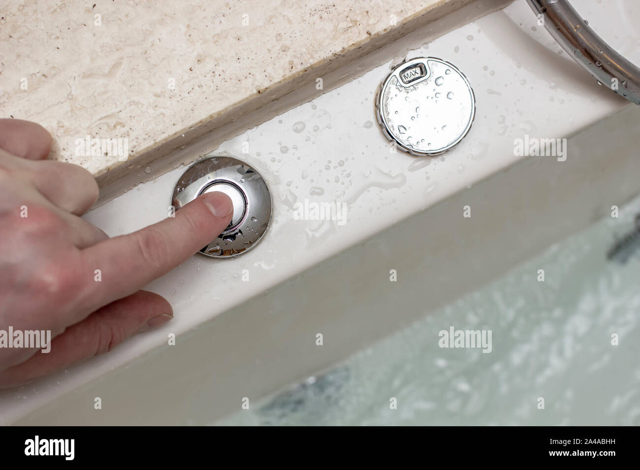 Male hand presses a control button on a modern, luxurious whirlpool bath with clear, warm water. Close-up. Stock Photo