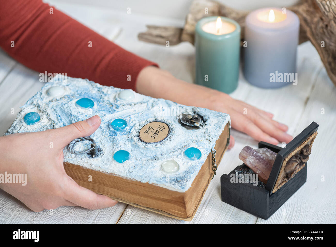 White magic book in a sorceress hand on a white wooden table background ...