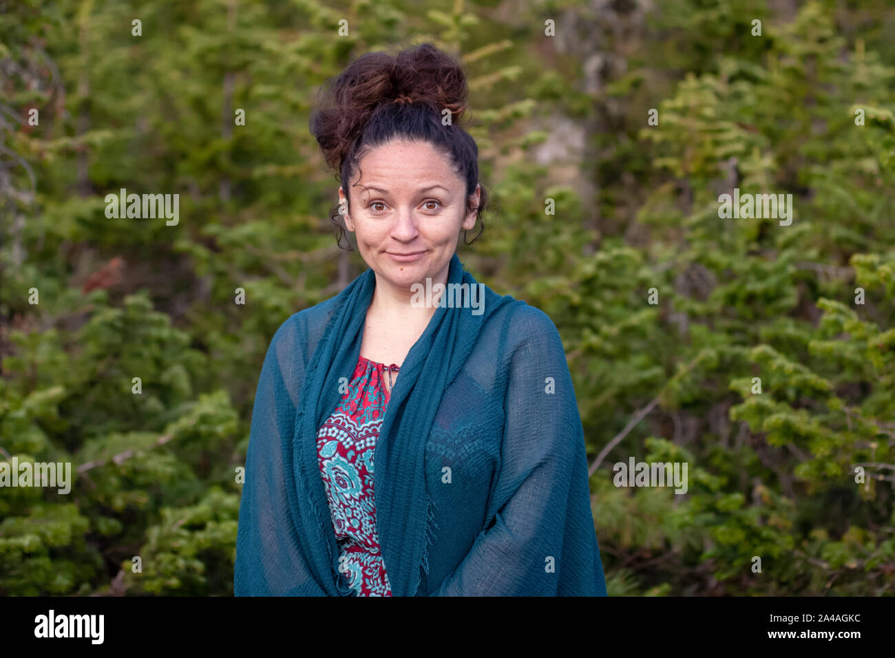 Portrait of a cute European girl with a surprised expression on her face with a blue scarf on her shoulders against the background of a coniferous blu Stock Photo