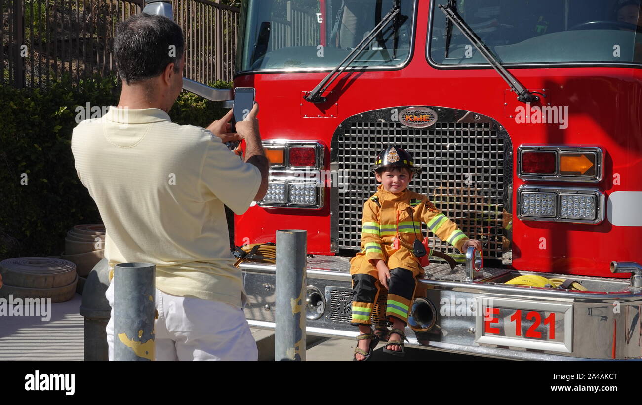 A dad takes a picture of his little boy sitting on a fire truck at fire station open house Stock Photo