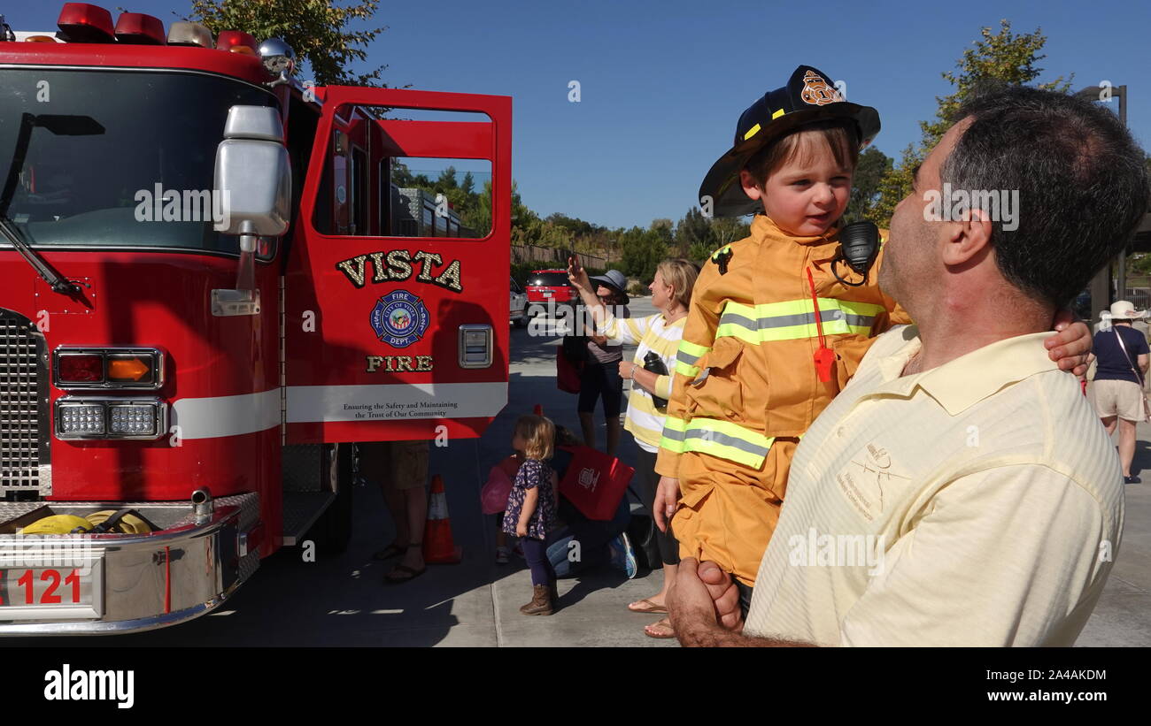 A dad carries his little boy dressed up as firefighter, as they explore the trucks at fire station open house Stock Photo