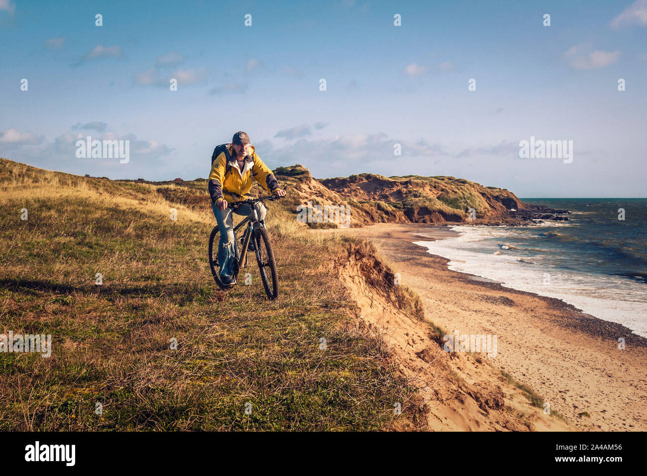 Cycling Ireland. Recreational cyclist with mountain bike and backpack riding on the edge of the sand dunes. Stock Photo