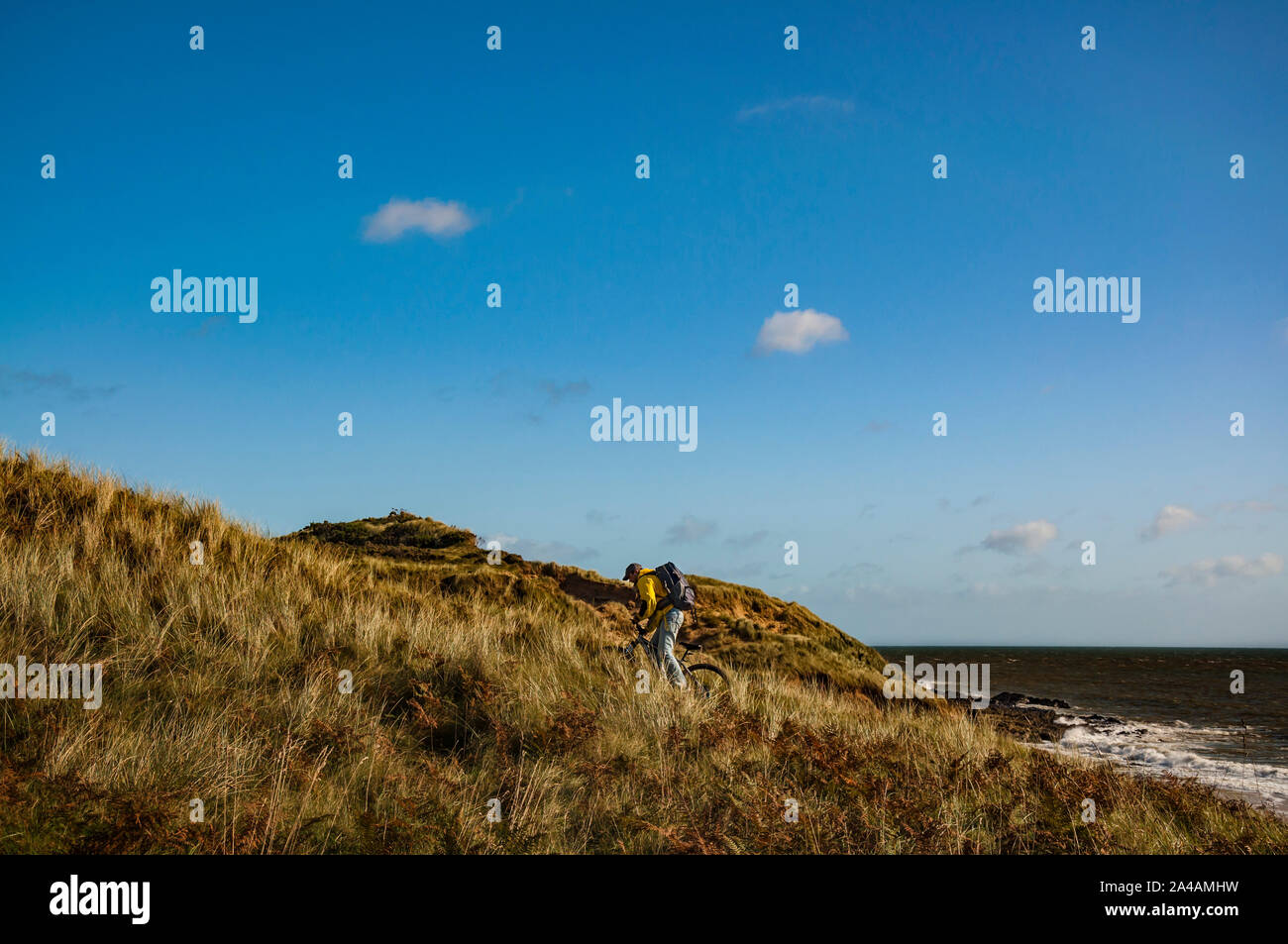 Cycling Ireland. Recreational cyclist with mountain bike and backpack riding uphill in sand dunes. Stock Photo