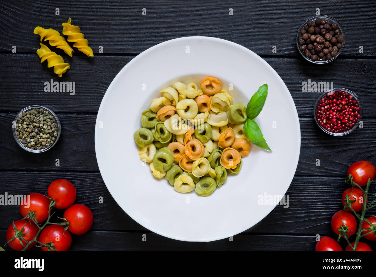 Vegetarian tortellini with cheese, tomatoes an spinach. Tasty italian cuisine on black wooden background. Cherry tomatoes and different kinds of peppe Stock Photo