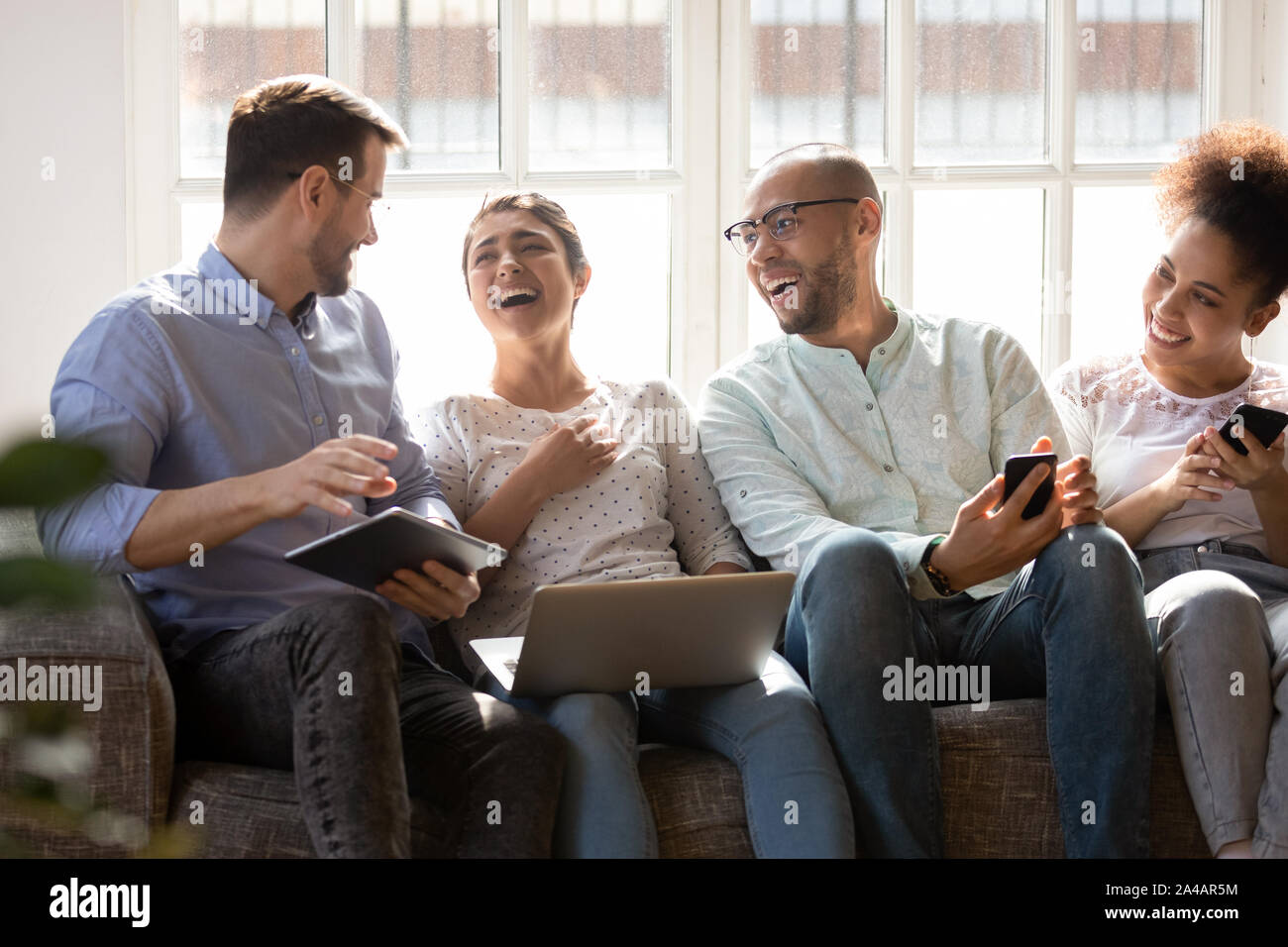 Happy diverse friends laughing at funny joke, using electronic devices Stock Photo