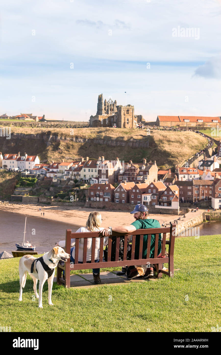 Man and woman with anxious dog overlooking the East Cliff beach below Whitby Abbey and The Church of Saint Mary Stock Photo