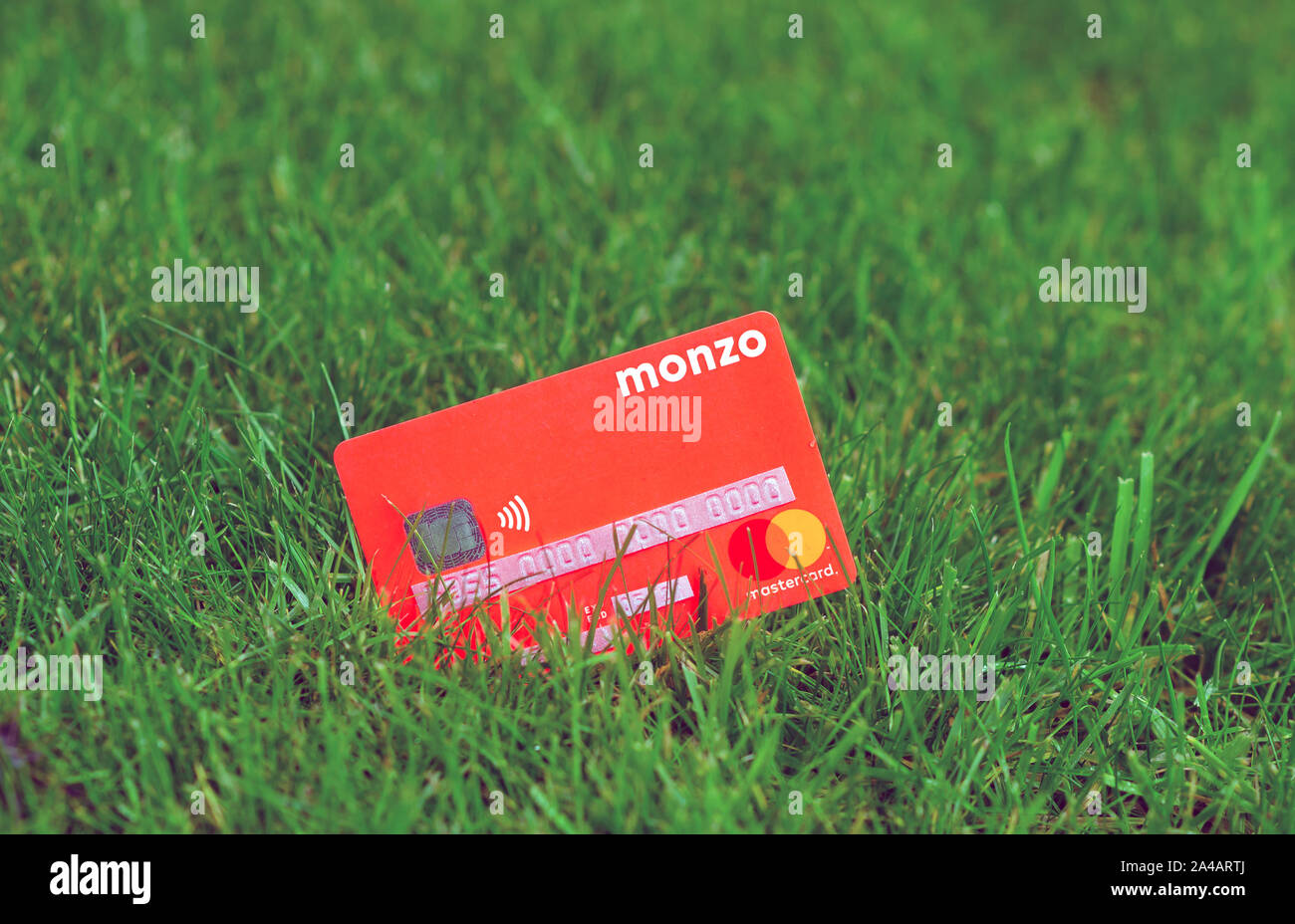 MONZO bank card on the grass. All sensitive information on the card is covered by stickers with dummy numbers. Stock Photo