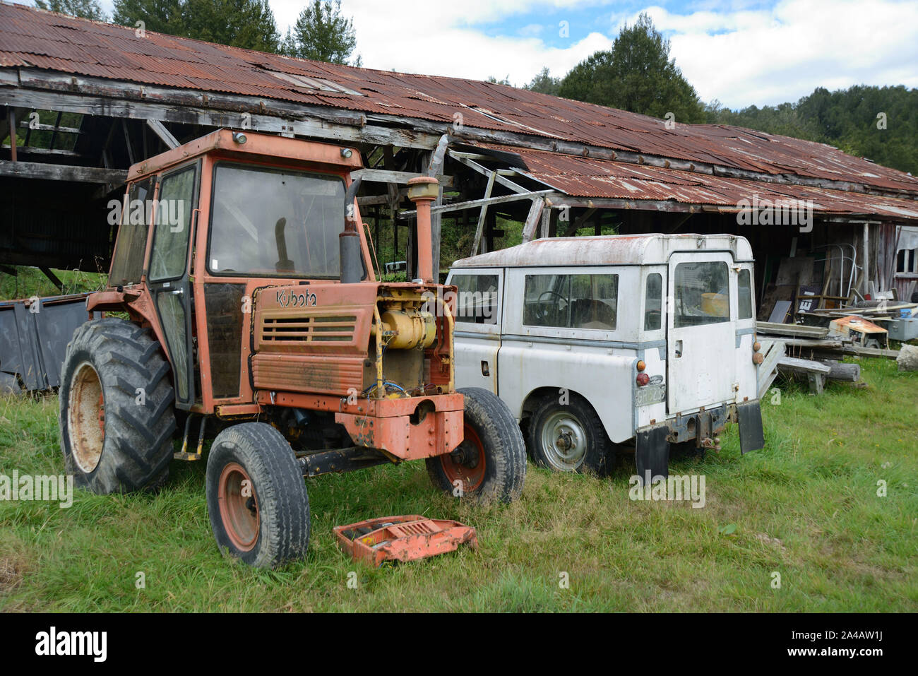 An abandoned tractor and 4WD rests near a barn in New Zealand Stock Photo