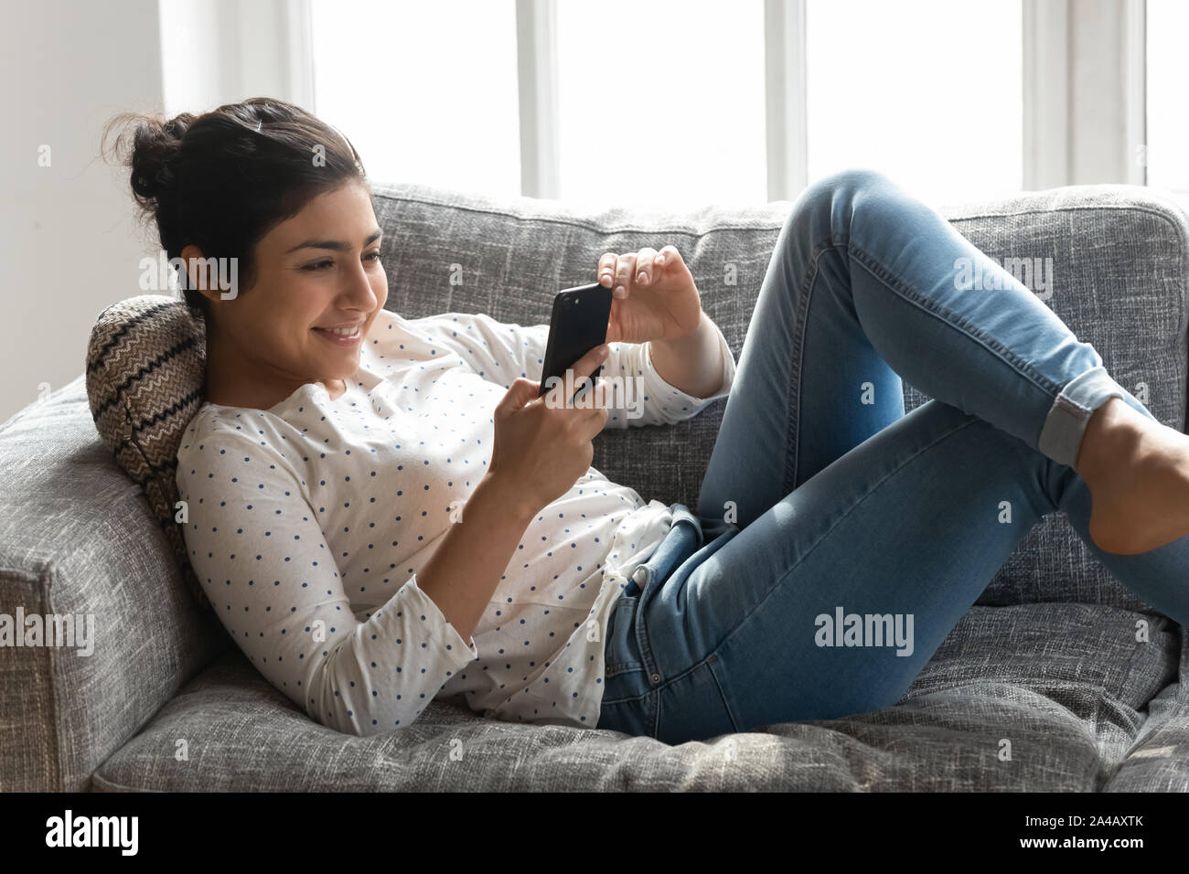 Happy Indian woman relaxing on couch at home, using phone Stock Photo ...