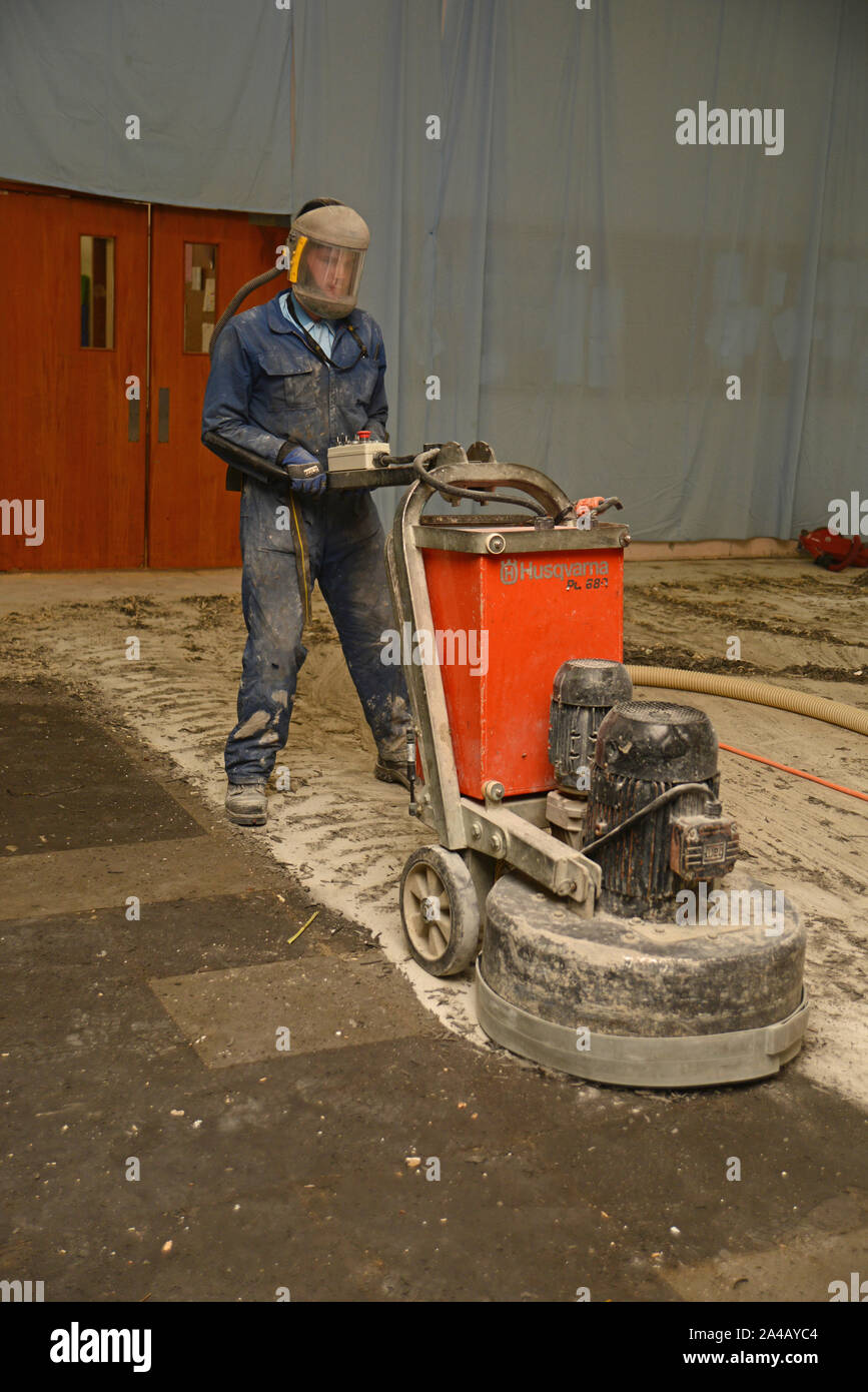 WEST COAST, NEW ZEALAND, JUNE 28, 2019: A tradesman uses a grinding machine to remove old carpet squares from a floor in preparation for new floor cov Stock Photo