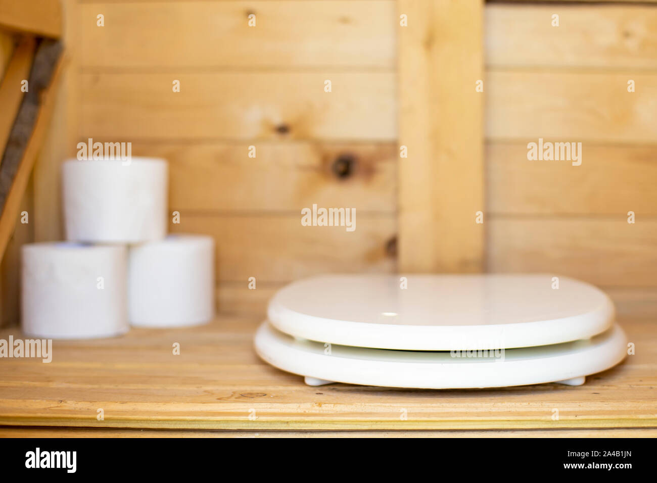 Modern toilet seat of white color in a rustic, wooden restroom (WC), in the background rolls of paper. Close-up. Stock Photo