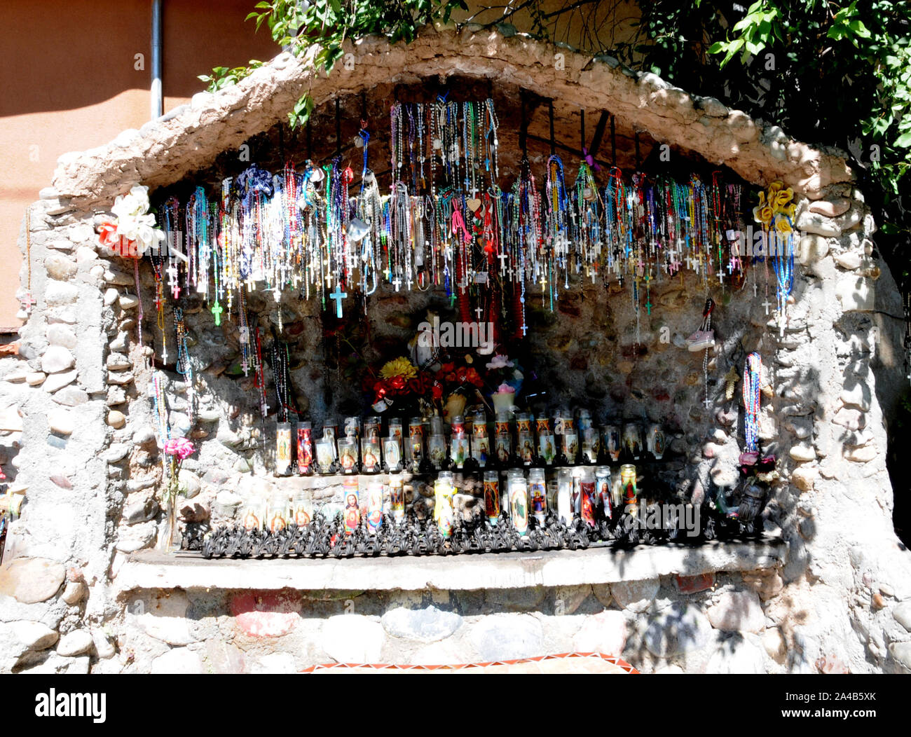 Offerings of crucifixes and candles in a small man made grotto at El Santuario de Chimayo, New Mexico. The church and grounds is an area of pilgrimage Stock Photo