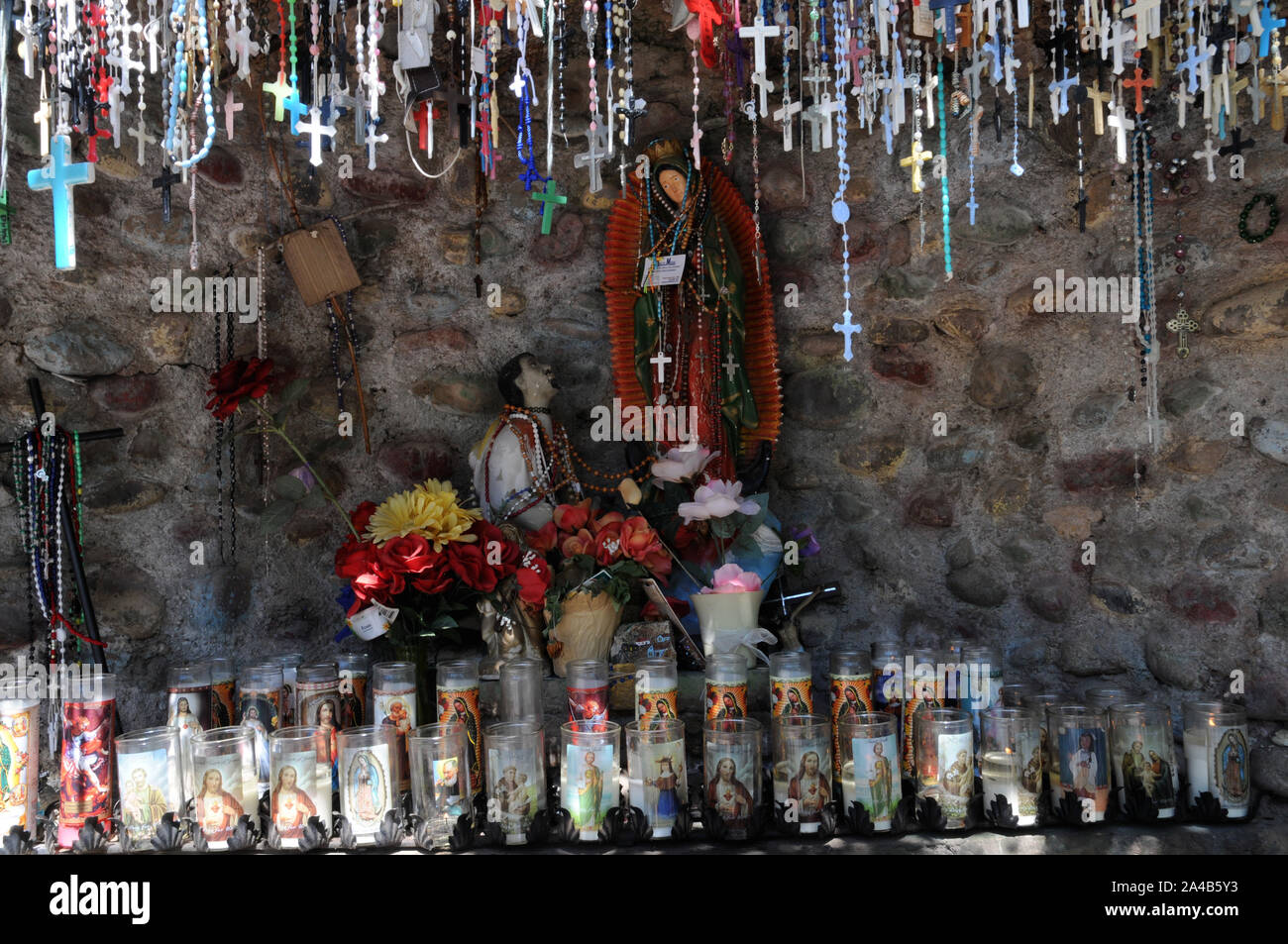 Offerings of crucifixes and candles in a small man made grotto at El Santuario de Chimayo, New Mexico. The church and grounds is an area of pilgrimage Stock Photo