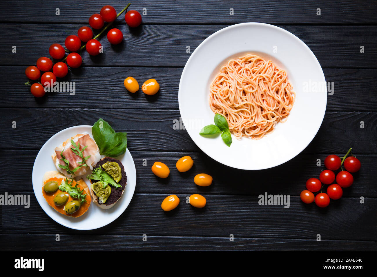 Tomato pasta with cheese, basil, red, orange and yellow cherries tomatoes on a black wooden background, top view. Bruschetta with ham and vegetables o Stock Photo