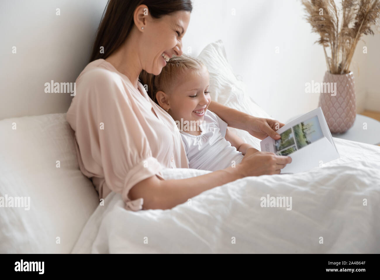 Mother reading book, funny story to little daughter in bed Stock Photo