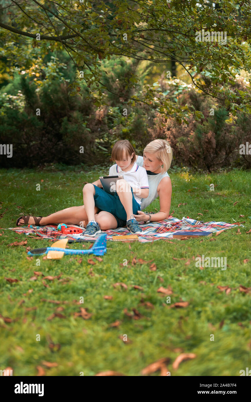 Young loving mother and her sweet son using a tablet on a park lawn Stock Photo