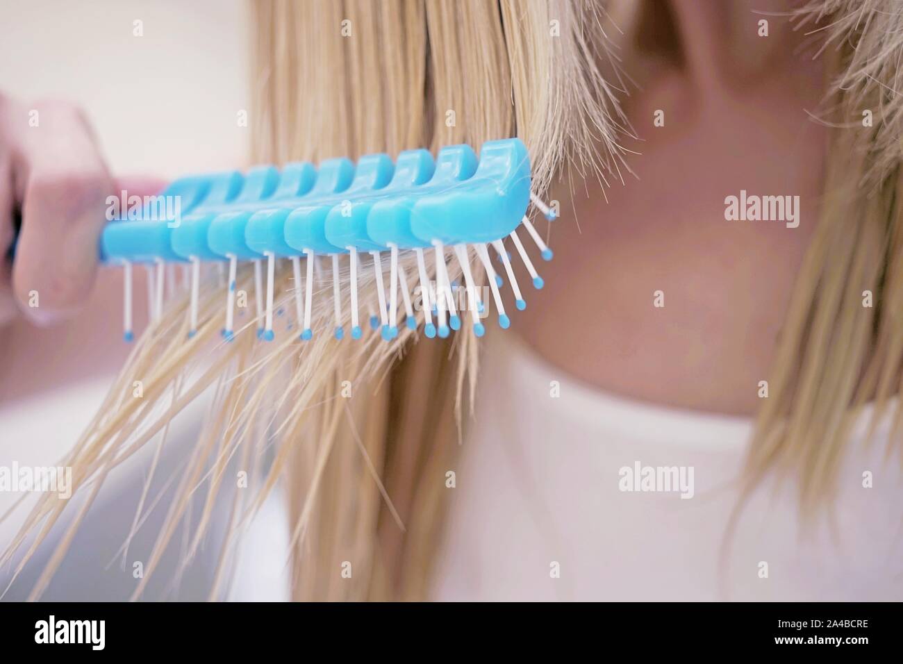 young girl combing her wet blond hair with a blue comb, close-up. Stock Photo