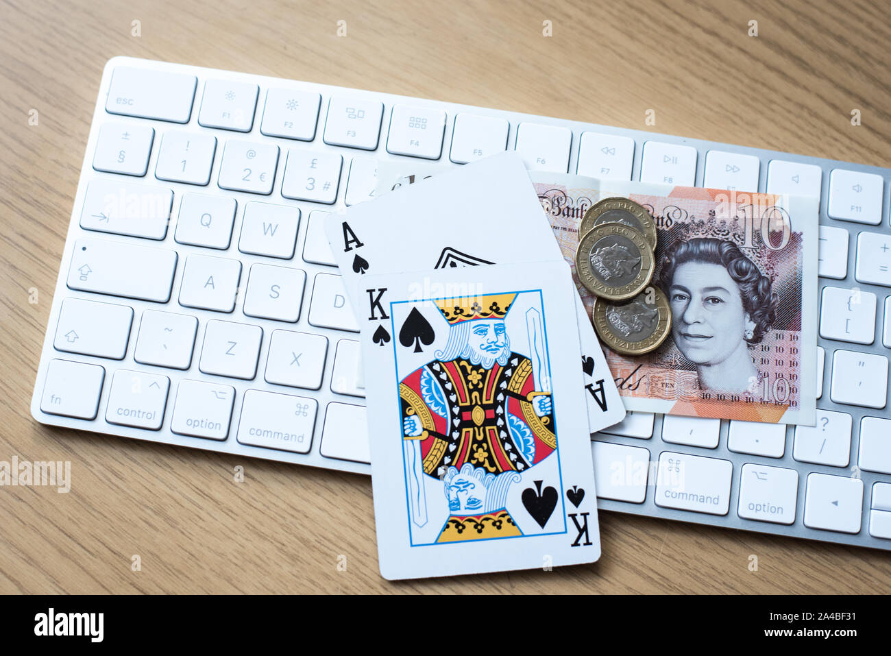 Online gambling and poker play concept with keyboard on a table with King and Ace cards alongside english currency and coins Stock Photo
