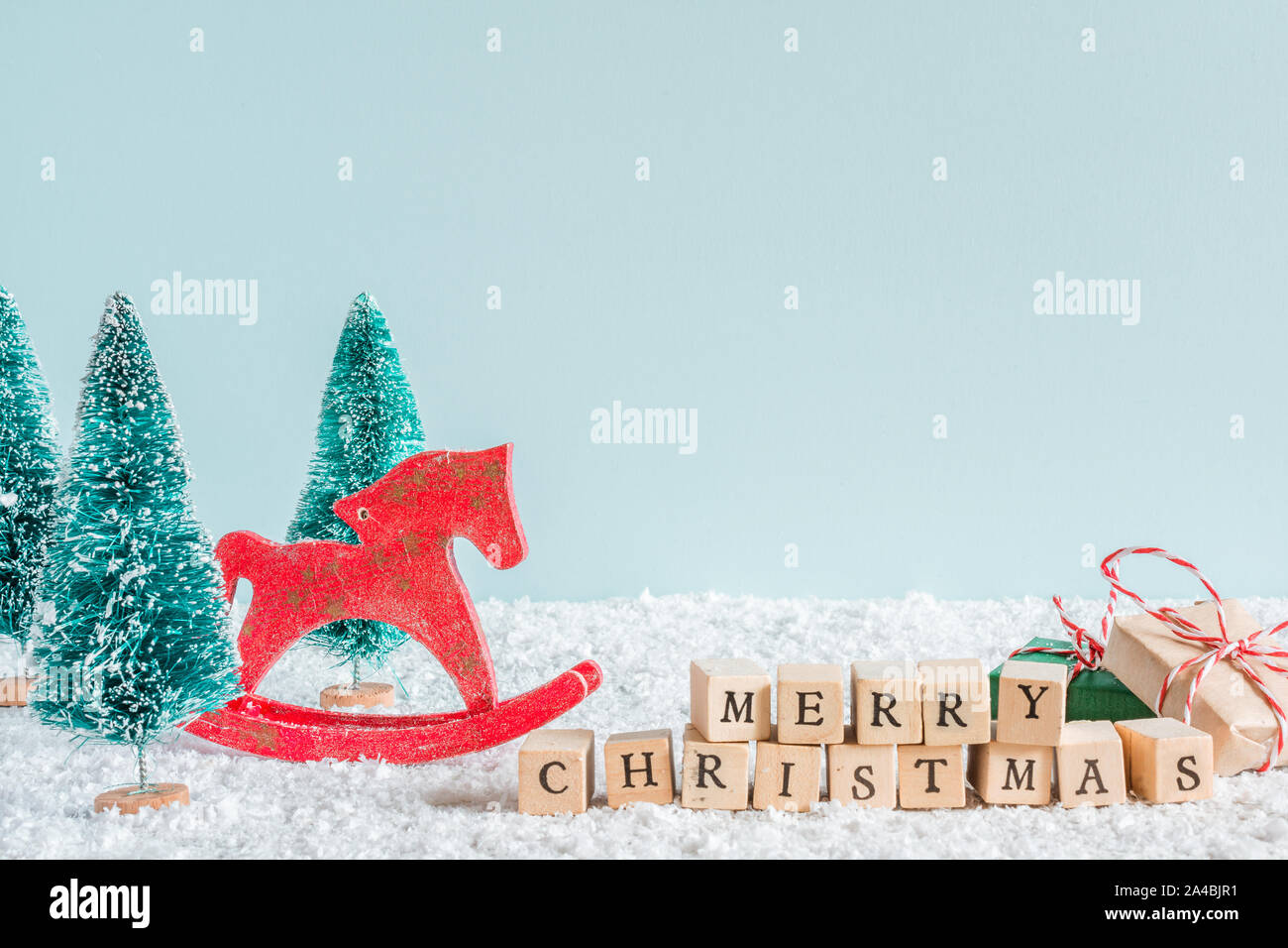 merry christmas inscription with fir trees, horse toy, gift boxes on snow background. creative christmas card with copy space Stock Photo
