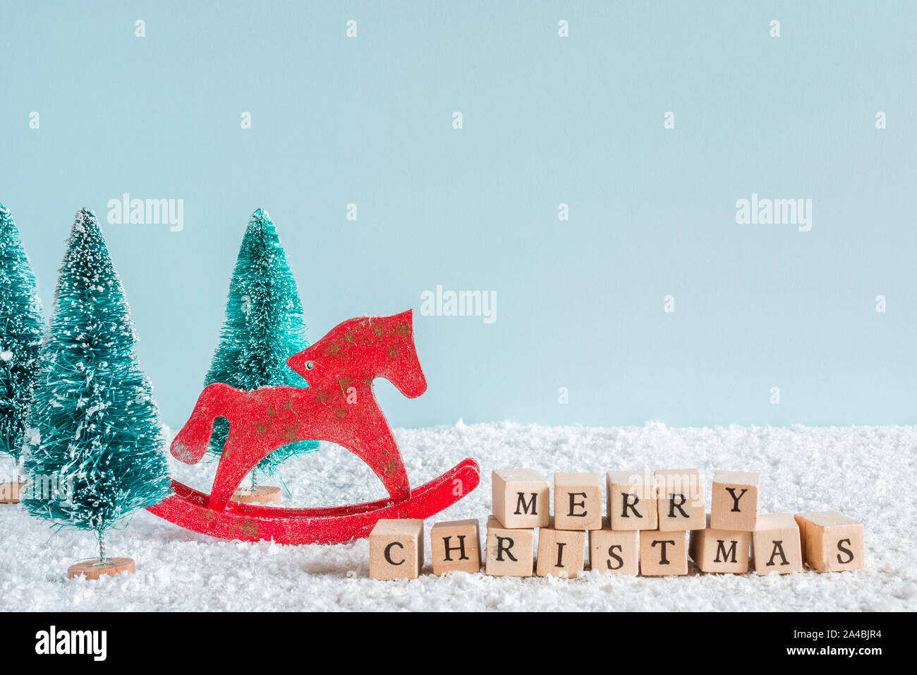 merry christmas inscription with fir trees and horse toy on snow background. creative christmas card with copy space Stock Photo