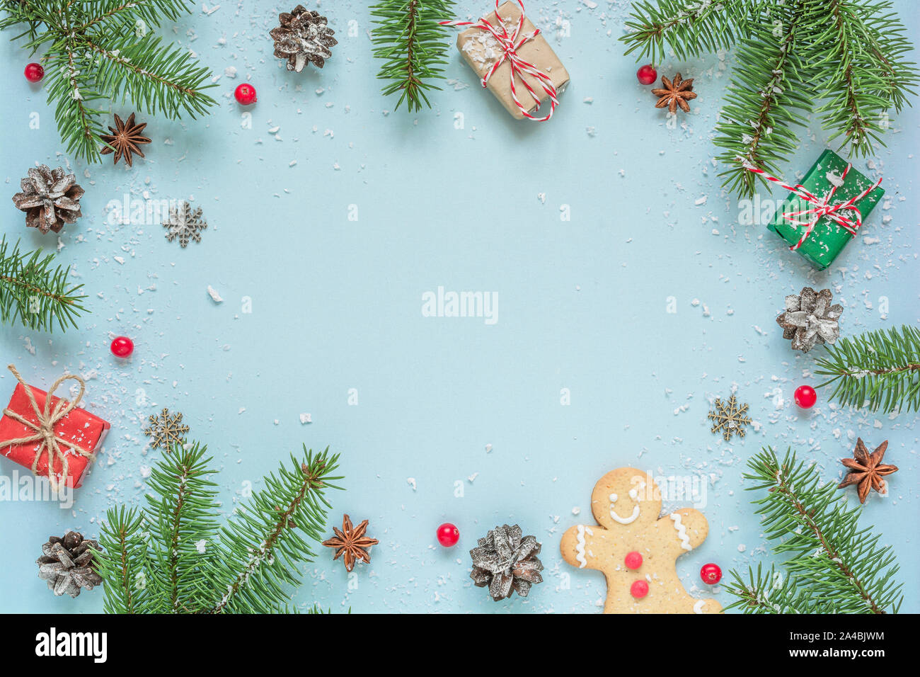 Christmas frame made of fir tree branches, decorations, berries, gingerbread and pine cones on blue background. Christmas background. Flat lay. top vi Stock Photo