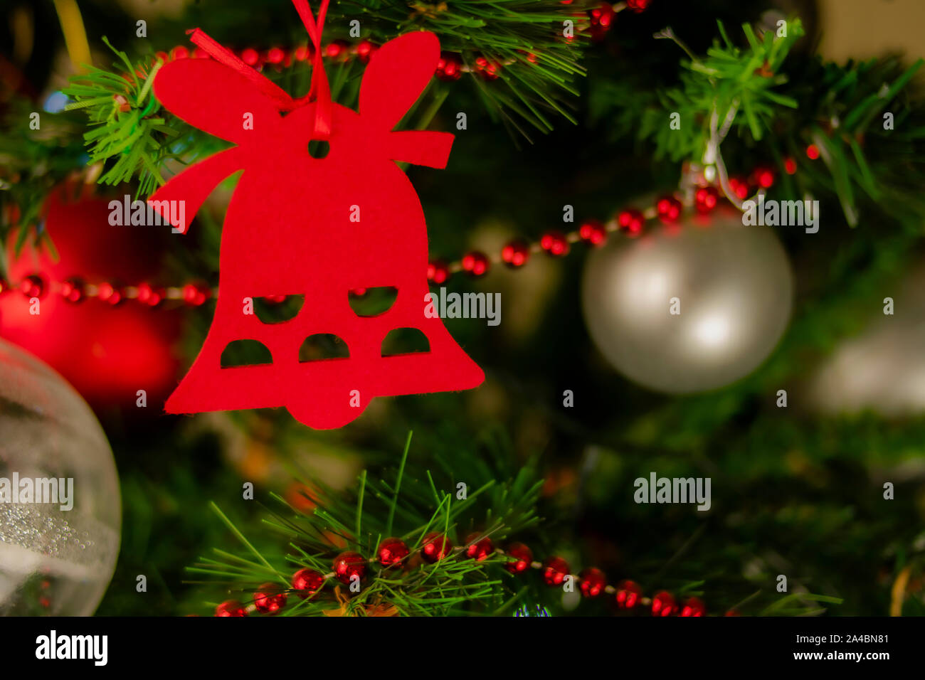 campana navideña cuelga de la rama del abeto de navidad entre bolas de colores plateados y rojos y una cadena de bolas rojas pequeñas. Stock Photo