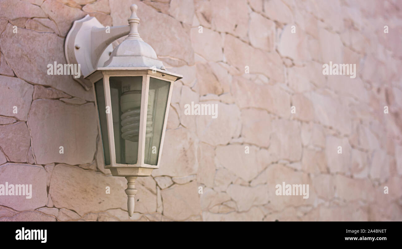 Hanging lamp on the side of a facade of a house and its garden, in a classic style, with glass and metal, and inside it spiral halogen bulb, the whole Stock Photo