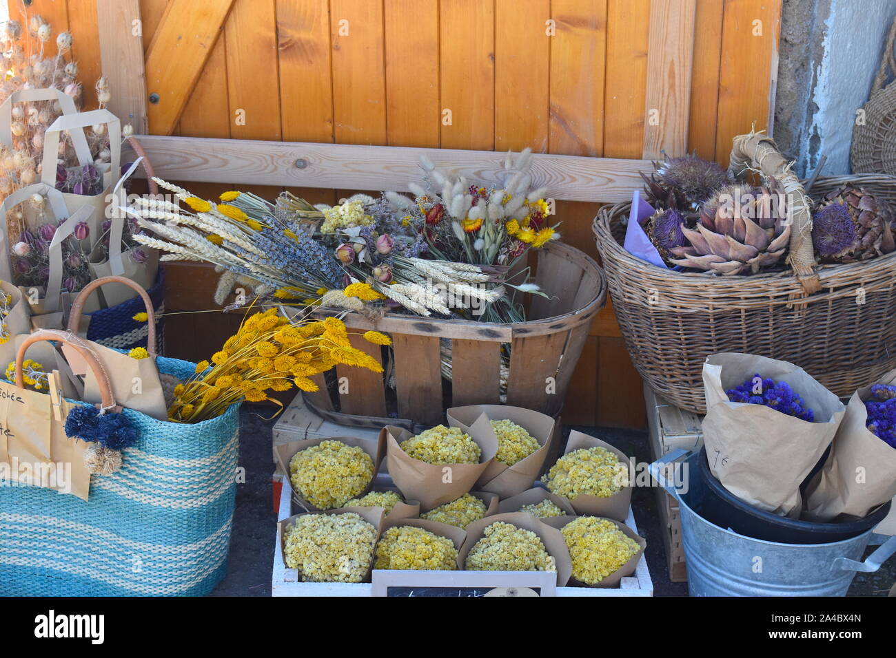 Vintage dried flowers for decoration, bouquets of wild flowers and straw beach hand bags on local market. Traditional French bargain items for sale Stock Photo