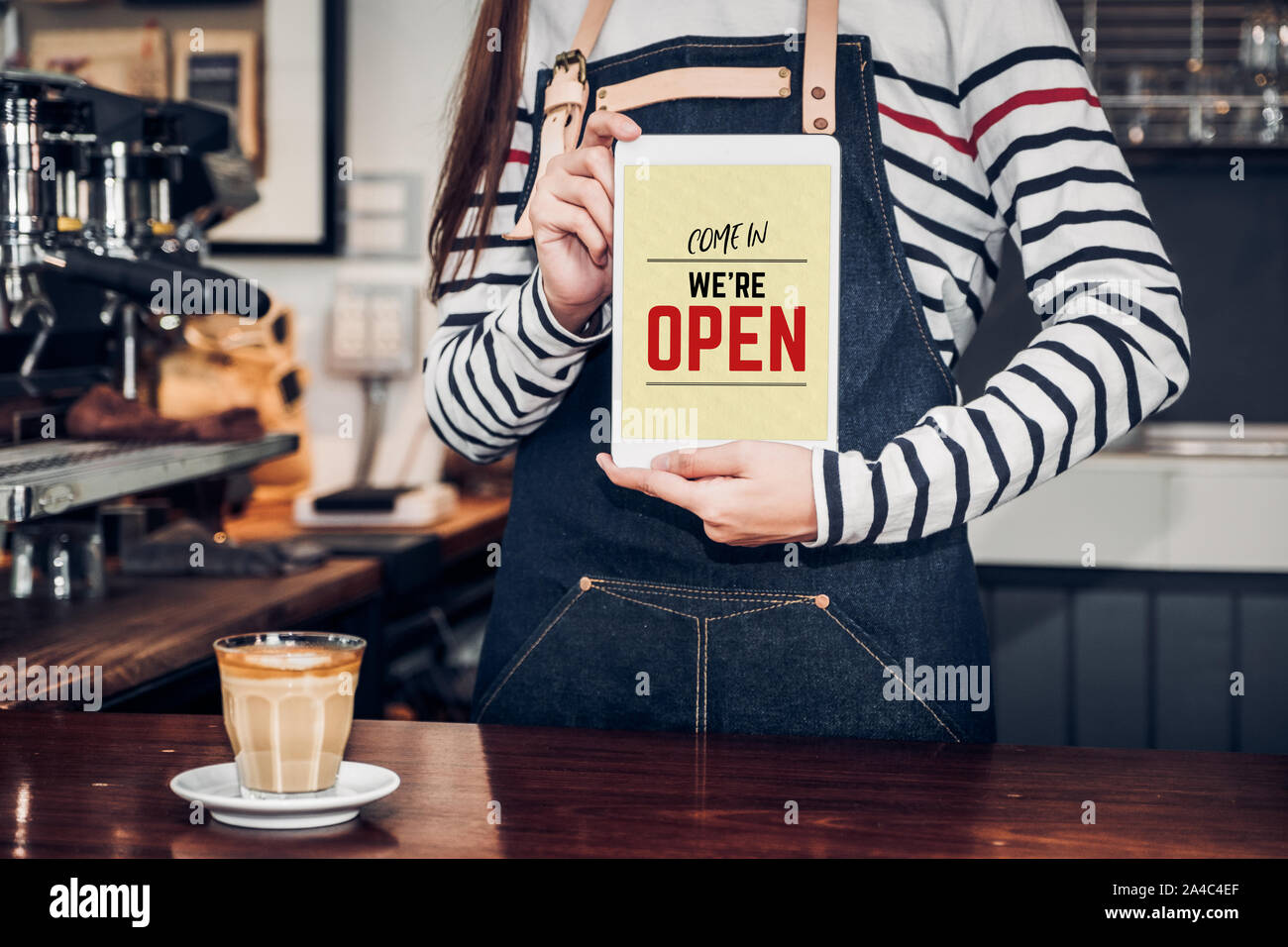 woman barista wear jean apron holding come in we are open sign on tablet to customer at bar counter with smile emotion,Cafe restaurant service concept Stock Photo